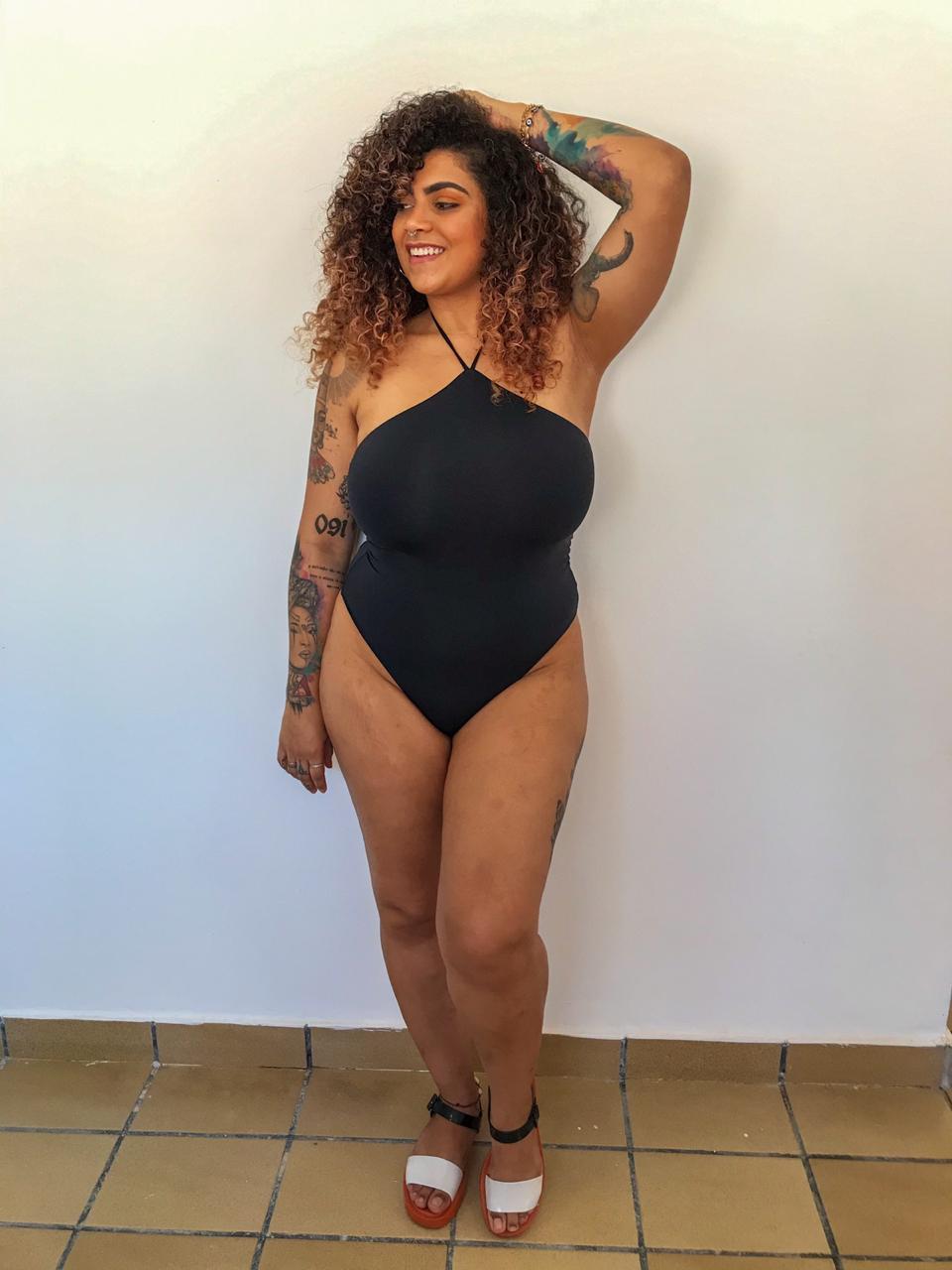 Modelo vestindo body preto justo com alça única transpassada, destacando decote assimétrico e acabamento liso.