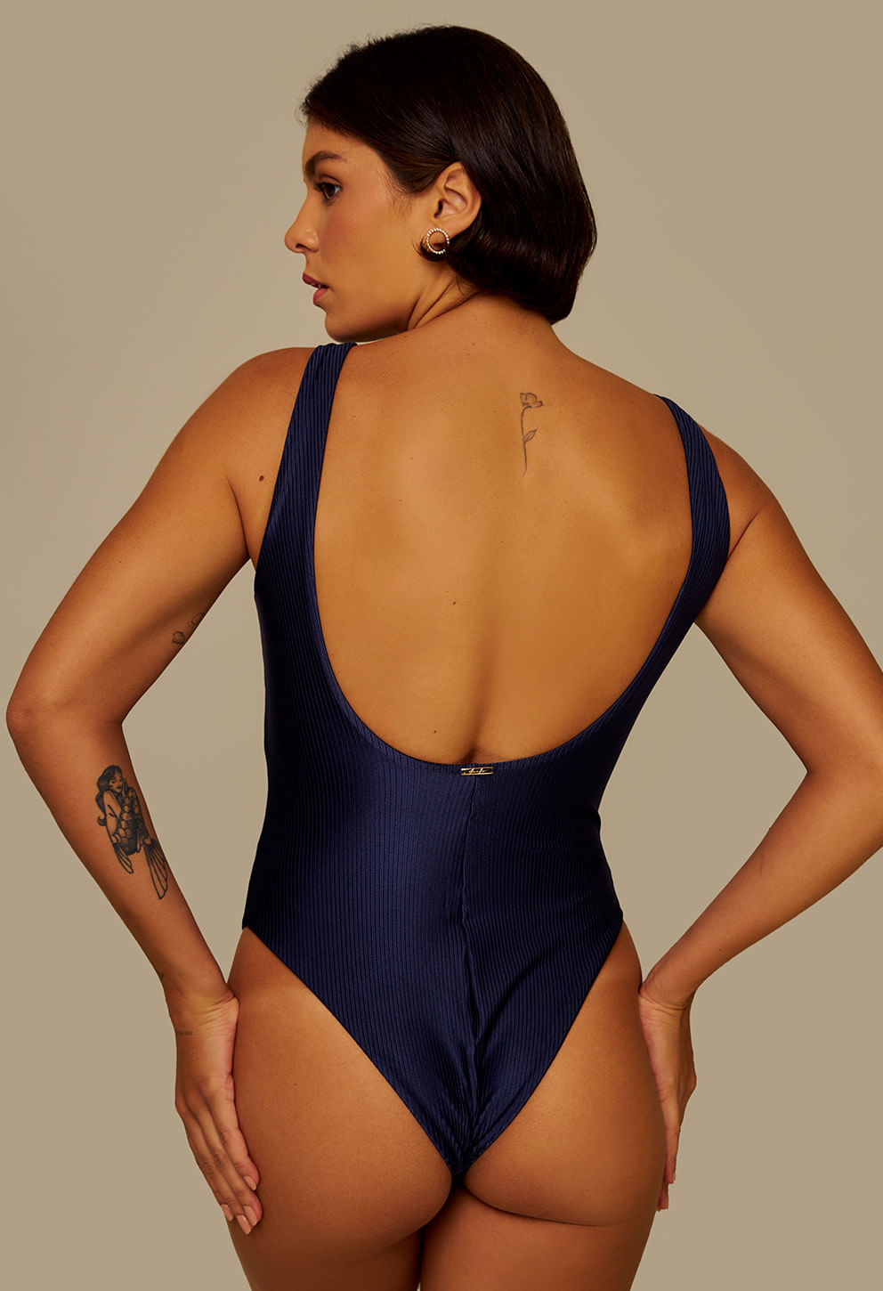 Vista traseira do body marinho com decote profundo nas costas e logo dourado