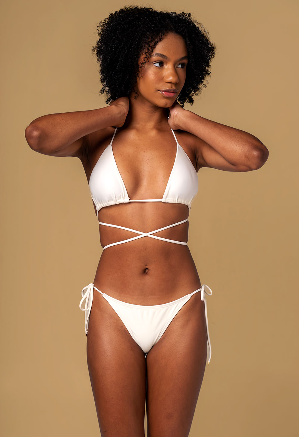 Modelo feminina com pele morena usa biquíni pérola, top cortininha com tiras finas e amarração