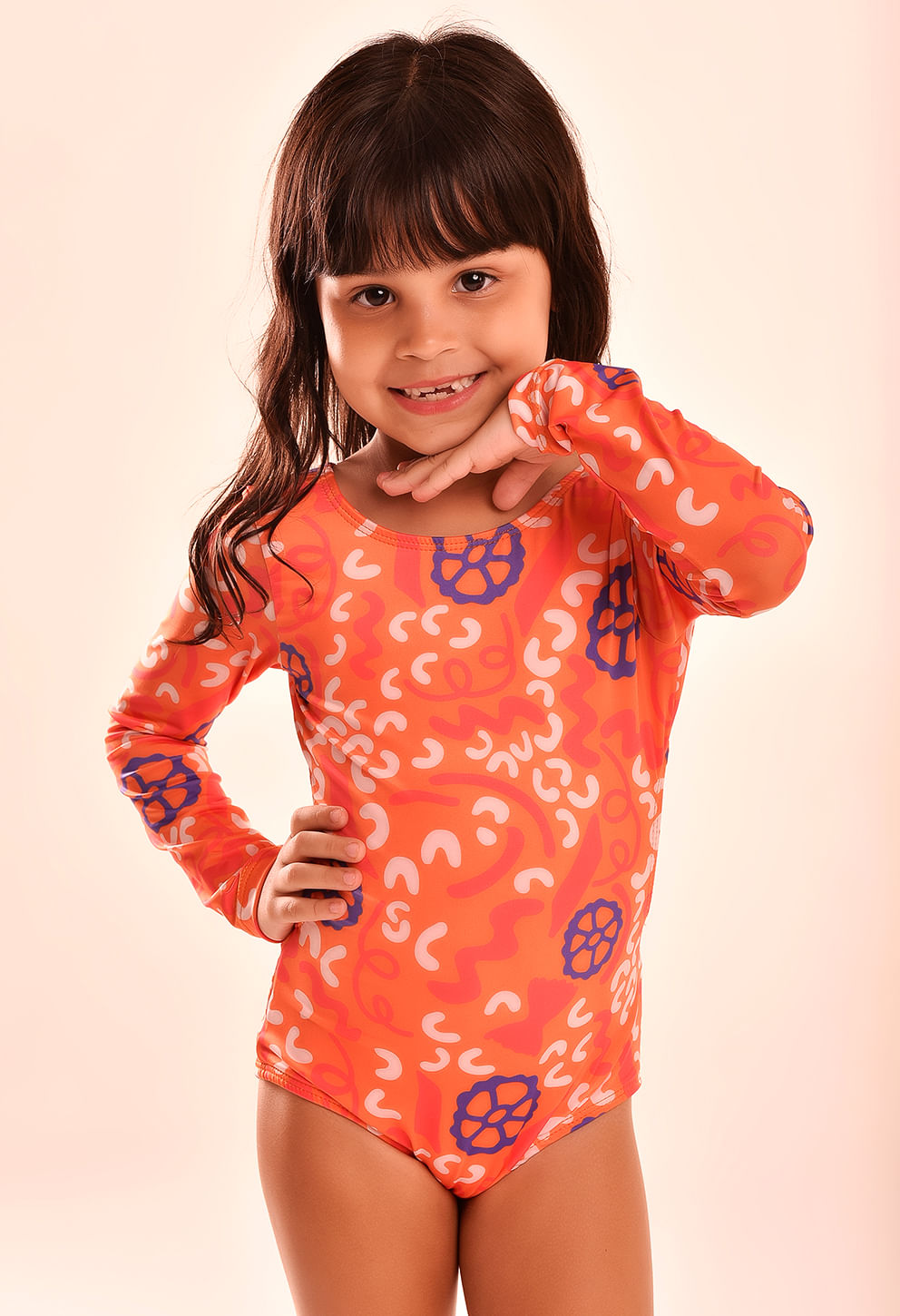 Menina sorridente vestindo maiô laranja de manga longa com estampa abstrata em branco e azul, mostrando design com amarração nas costas.