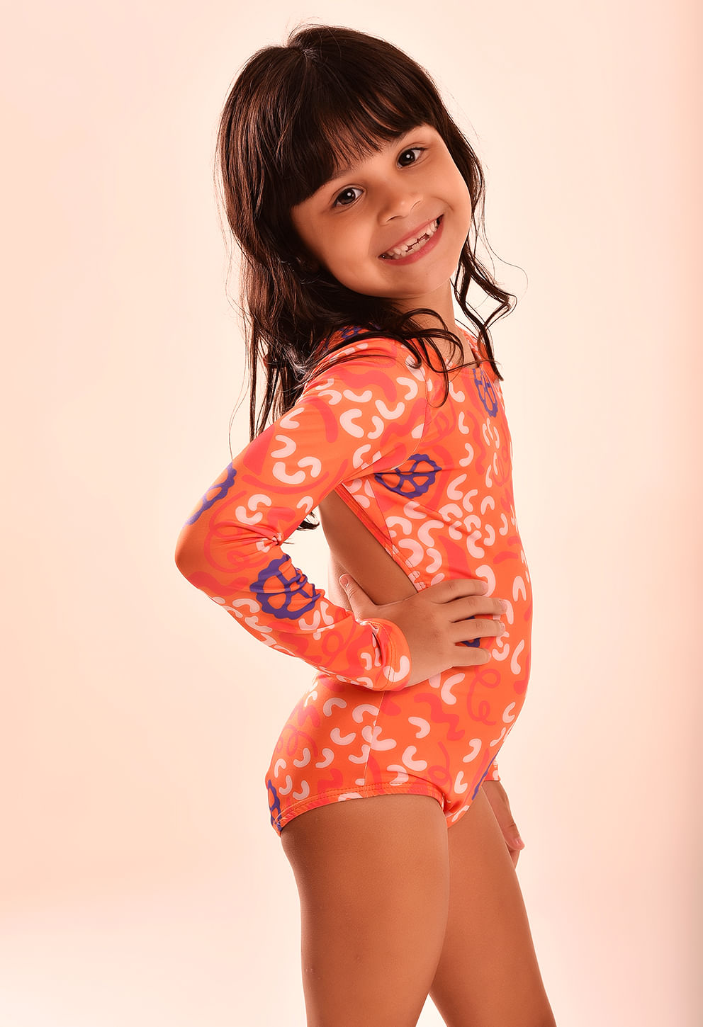 Menina de perfil mostrando o maiô laranja de manga longa com abertura nas costas e amarração no pescoço.