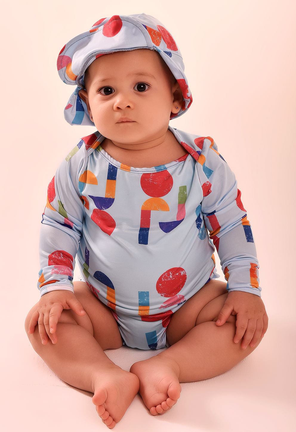 Bebê sentado usando camisa manga longa e chapéu bucket combinando em tom azul claro