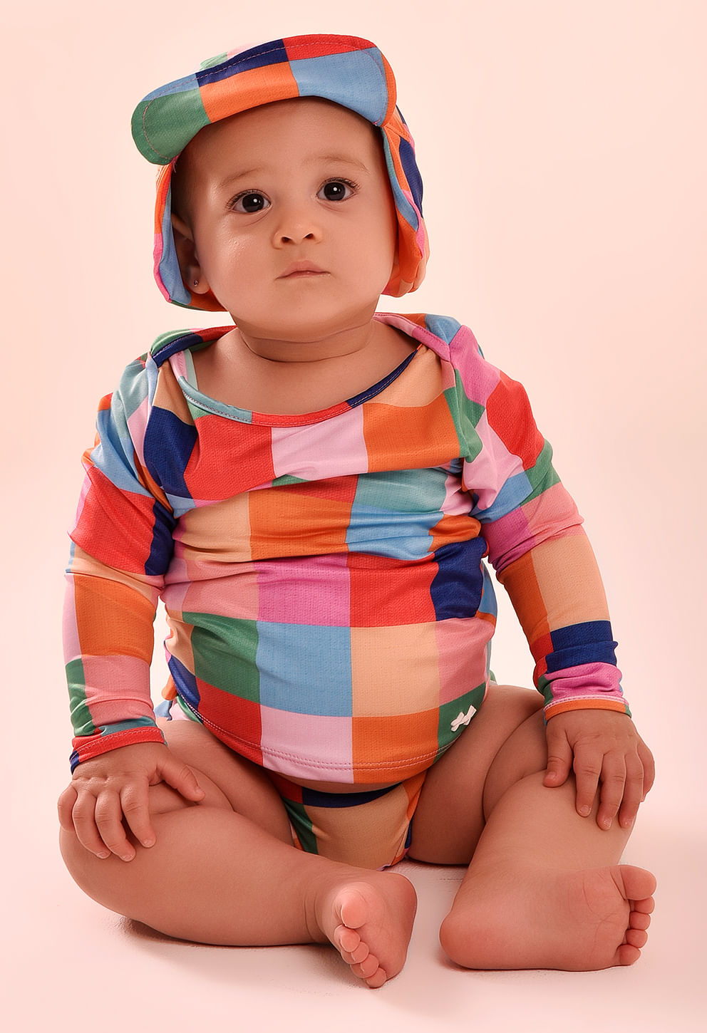 Bebê sentado vestindo camisa de manga longa com estampa quadriculada multicolor; gola redonda e punhos simples