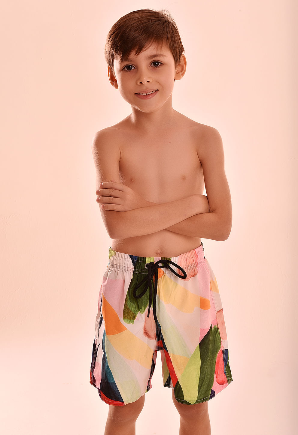 Menino usando bermuda infantil elástica com estampa colorida em tons de rosa, verde, laranja, amarelo, azul e vermelho