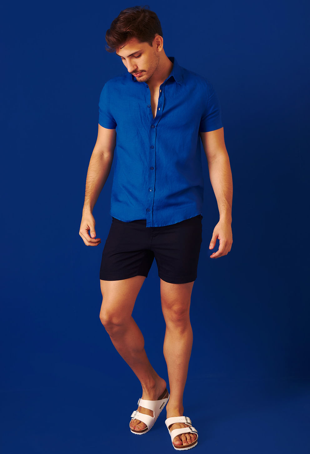Homem vestindo bermuda preta de linho com camisa azul royal, fundo azul