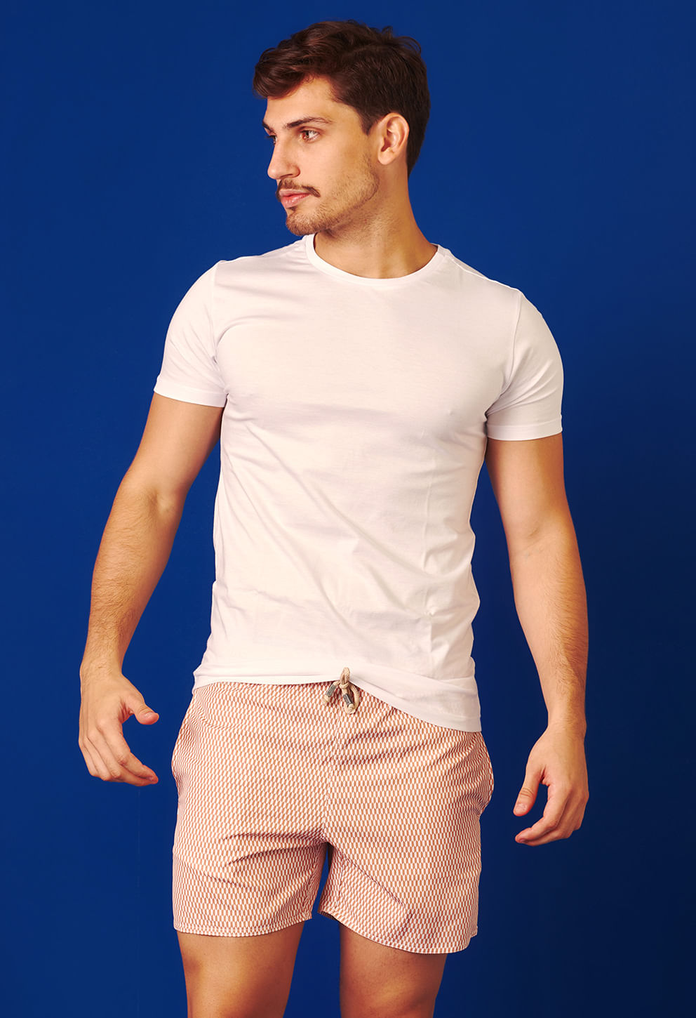 Homem de perfil usando bermuda casual shortinho geométrica em tons de vermelho e bege, com cordão ajustável
