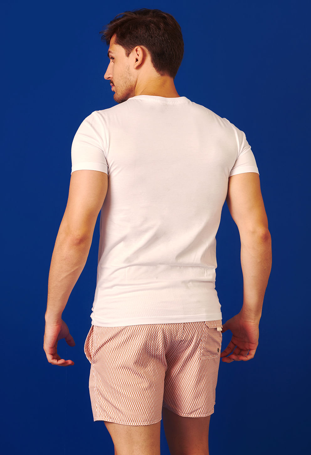 Homem visto de costas com bermuda casual shortinho geométrica e bolsos, fundo azul