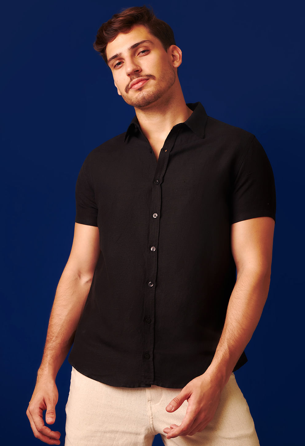 Modelo masculino usando camisa preta de manga curta, caimento reto em tecido leve
