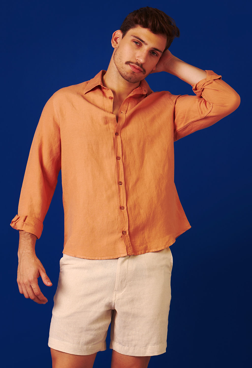 Homem em pose casual usando camisa coco queimado com fundo azul