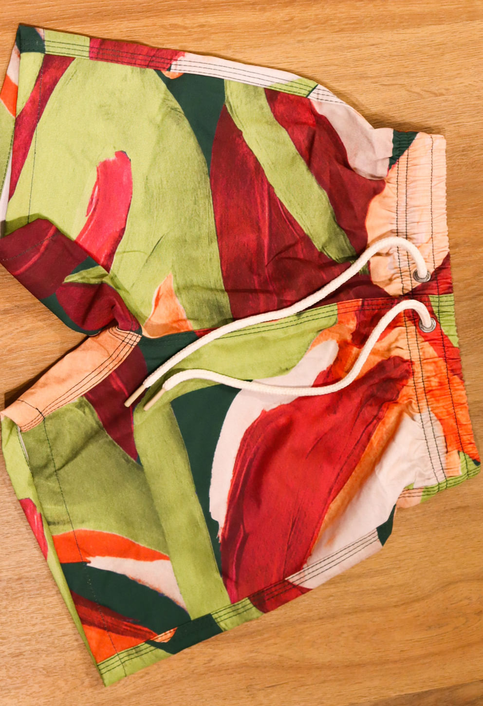 Bermuda infantil com elástico na cintura e cordão branco, estampa abstrata em vermelho, verde e laranja.