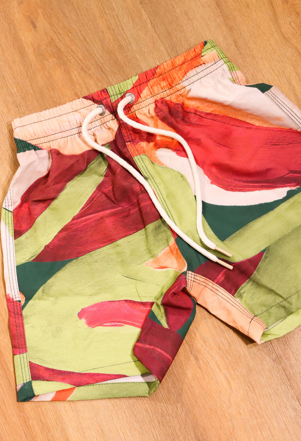 Bermuda infantil frente com estampa abstrata em vermelho, verde e laranja e cordão branco para ajuste.