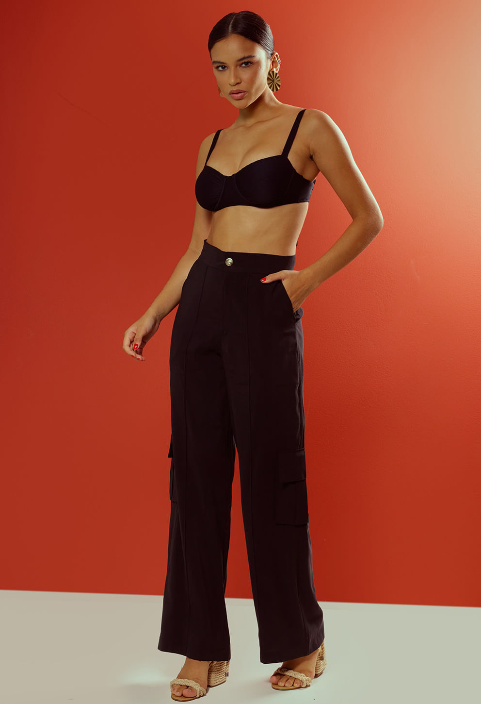 Calça pantalona preta com pregas frontais, bolsos cargo e botão dourado