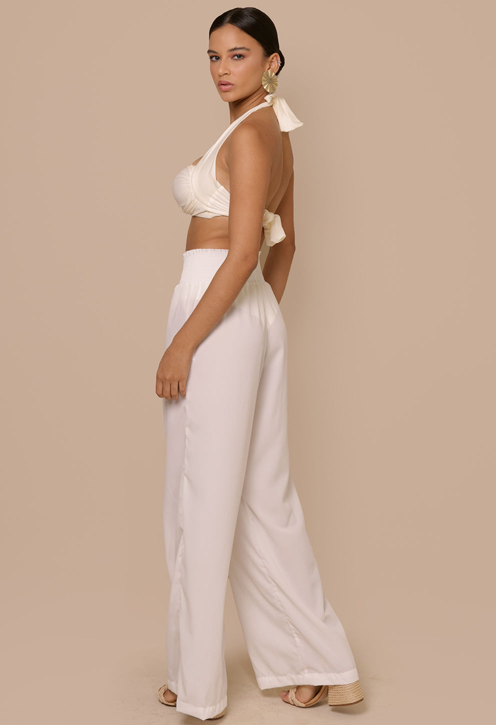 Imagem lateral da modelo vestindo calça pantalona Donatella Off White mostrando o cós largo e caimento