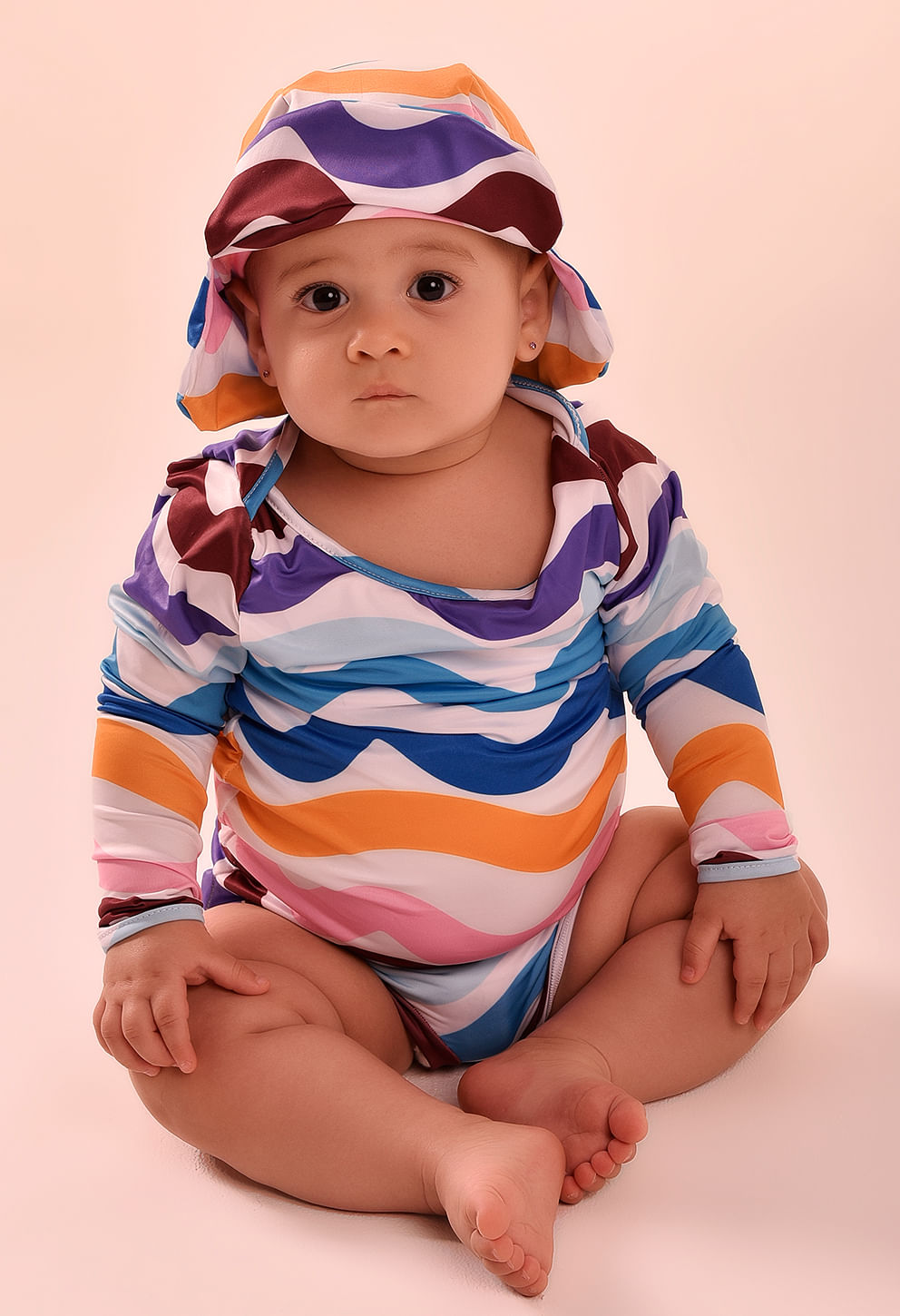 Bebê sentado com conjunto colorido laranja, azul e rosa, mostrando a calcinha bebê com estampa em ondas