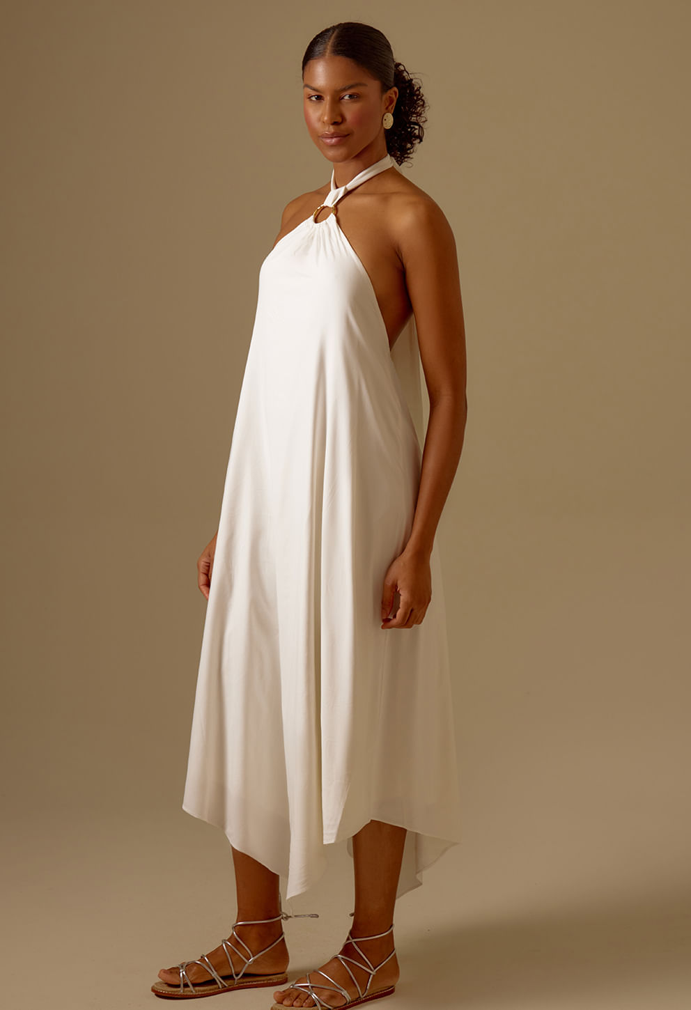 Modelo veste vestido Jaque off white com decote halter, argola dourada e barra assimétrica