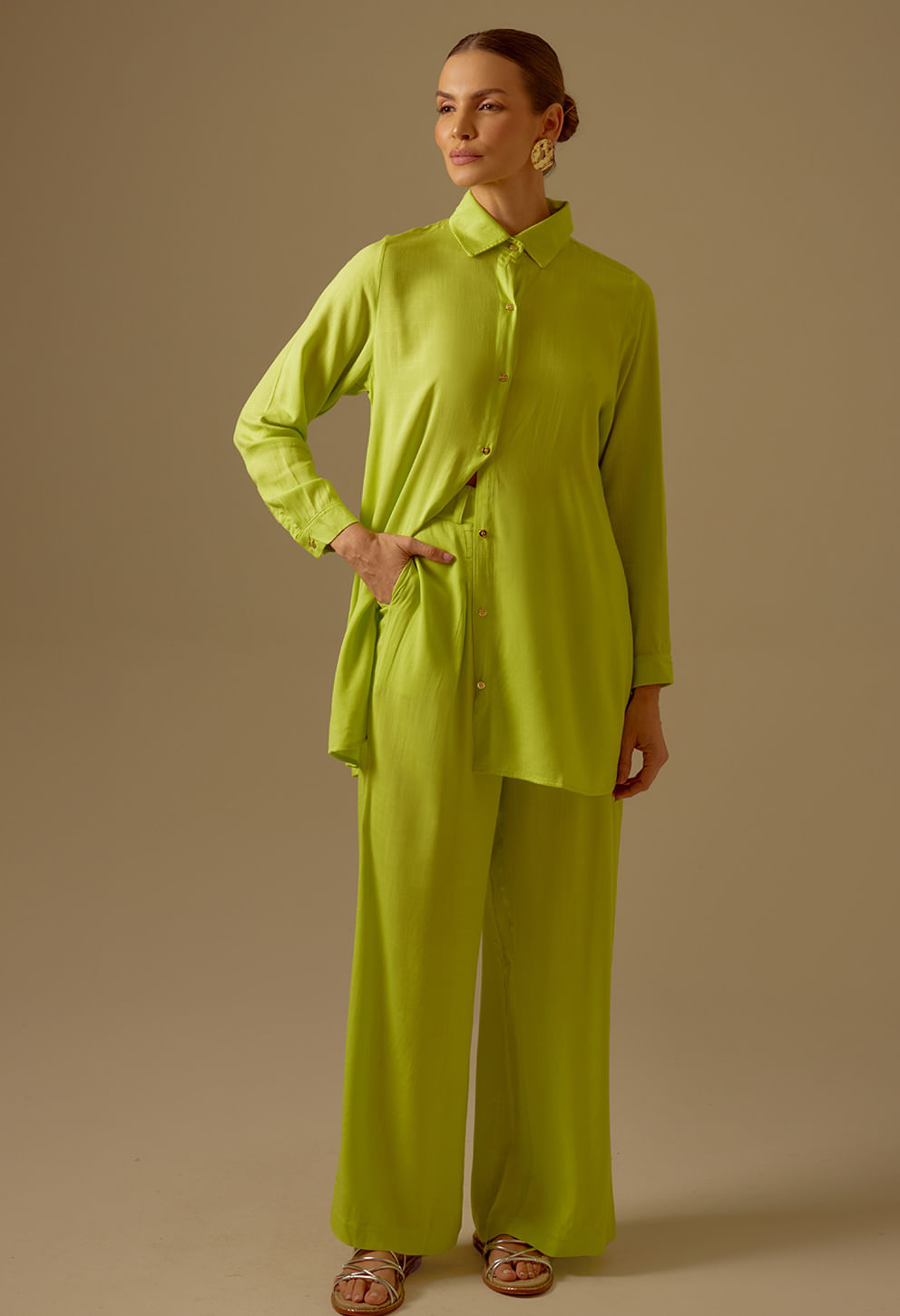 Mulher usando conjunto verde limão com calça pantalona e blusa camisa, fundo bege.