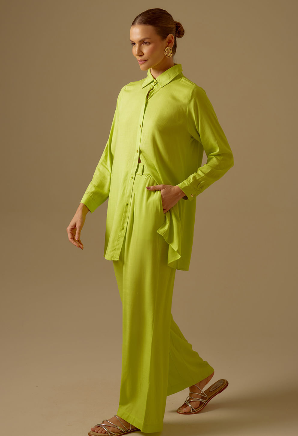 Perfil de mulher com calça pantalona verde limão e blusa camisa, mão no bolso.