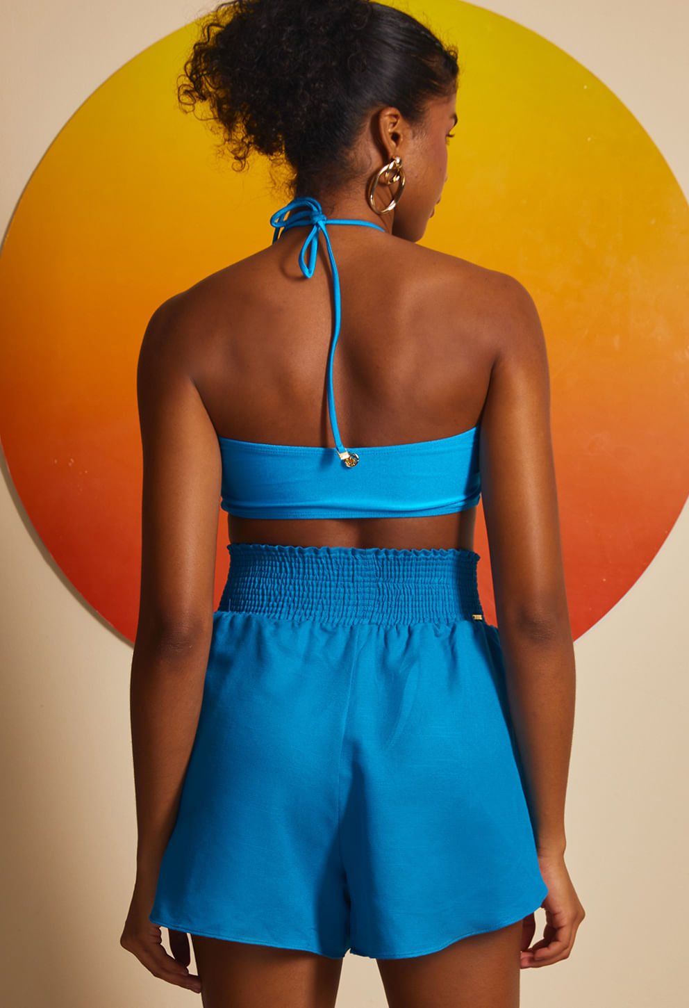 Modelo usando short azul transpassado traseira com elástico e bolsos