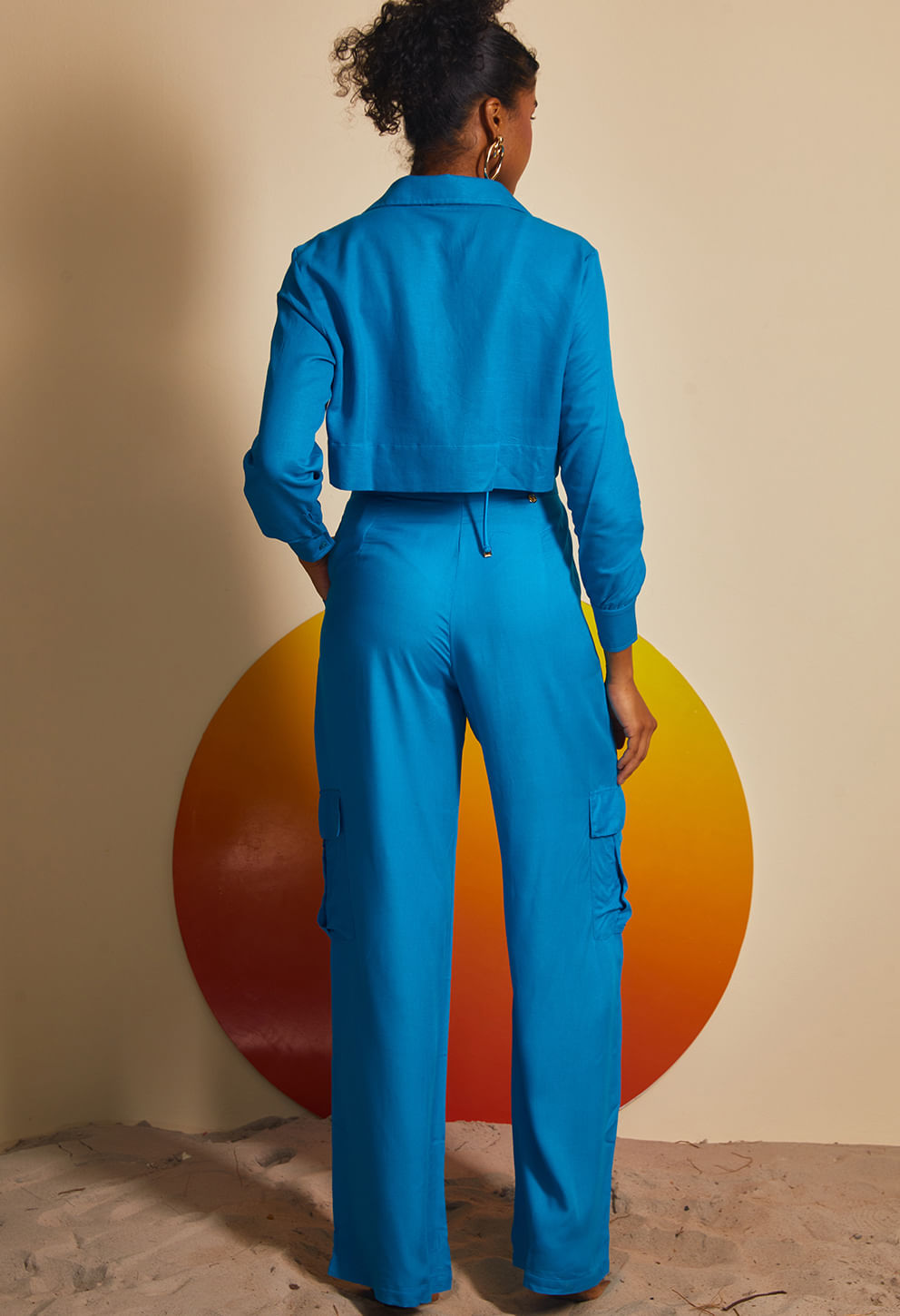 Vista traseira de mulher usando camisa cropped azul vibrante com detalhe de amarração na parte de trás