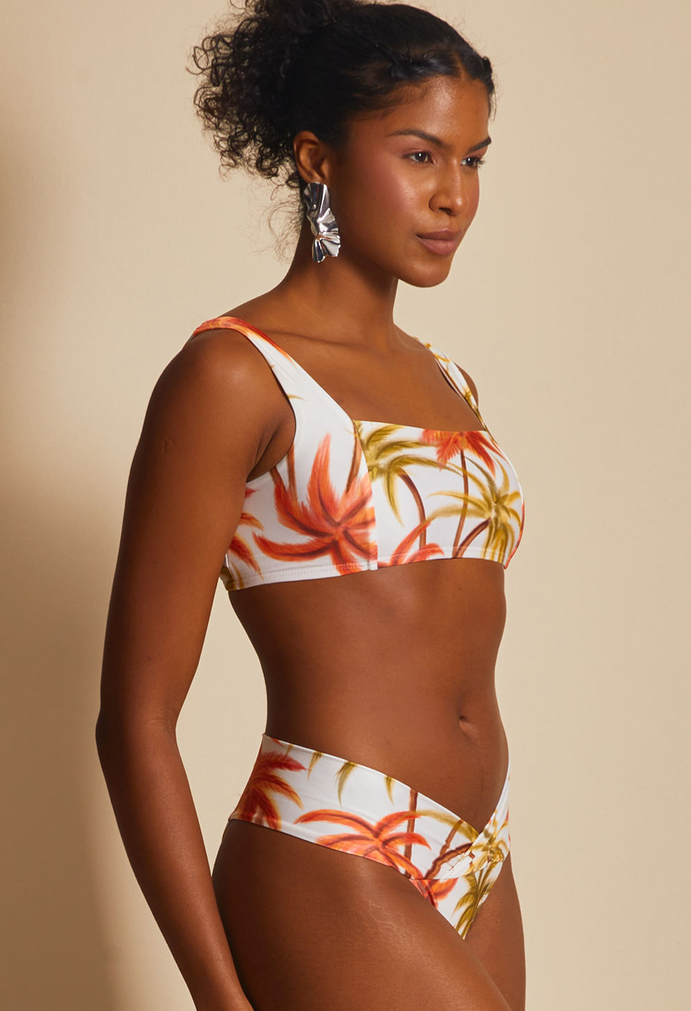 Imagem lateral de modelo vestindo calcinha pala dupla com estampa tropical em laranja, amarelo e verde