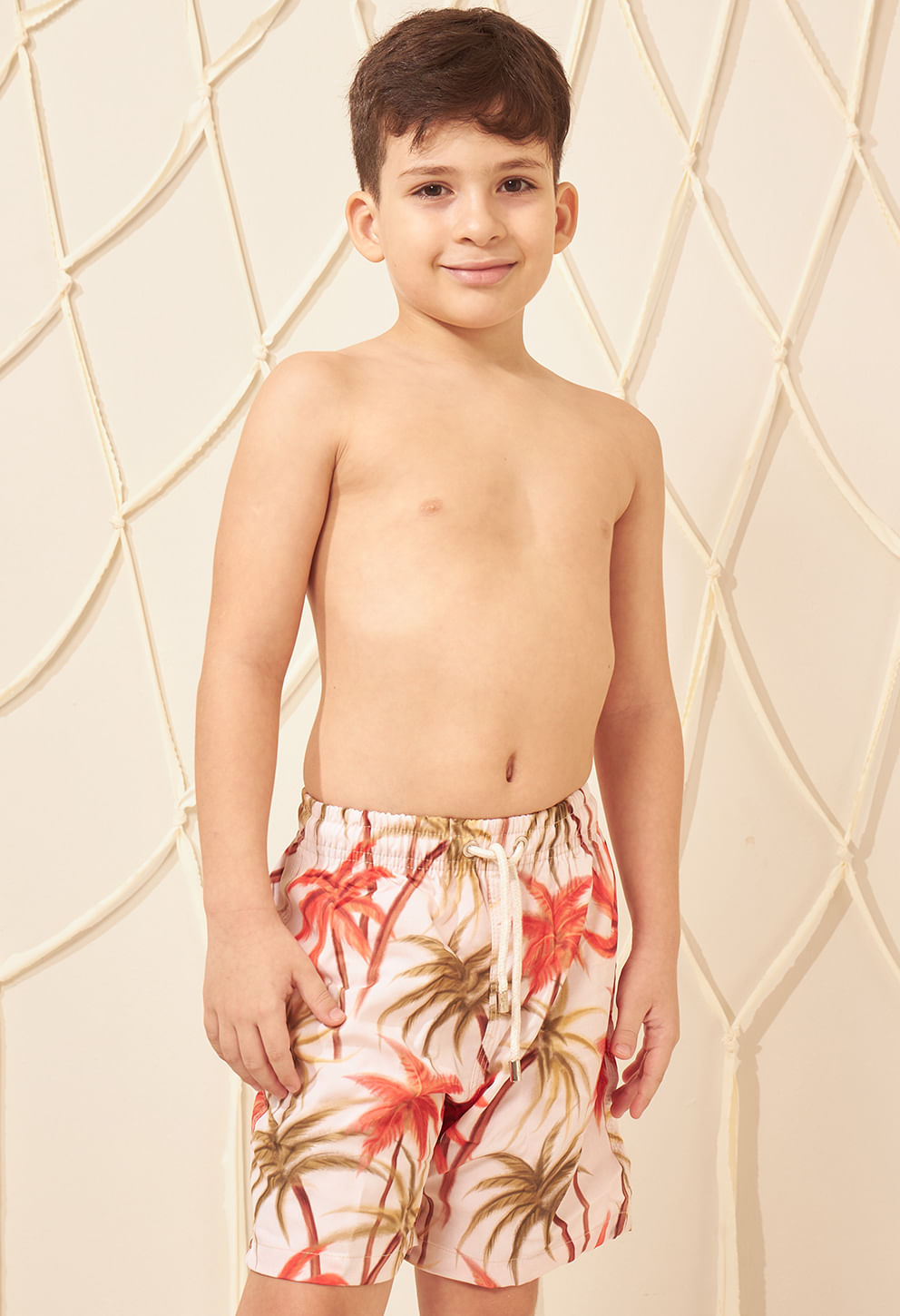 Menino sorridente usando bermuda infantil estampada tropical em branco com coqueiros