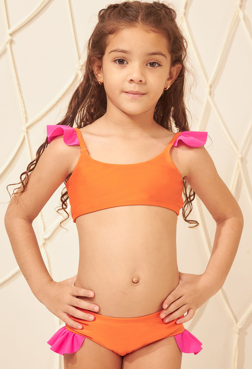 Menina infantil usando biquíni laranja com detalhes em babados rosa nas alças do top e nas laterais da calcinha.