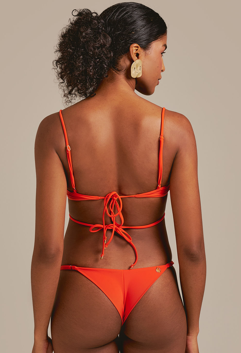 Vista traseira da calcinha semi fio laranja com regulador e detalhe metálico dourado