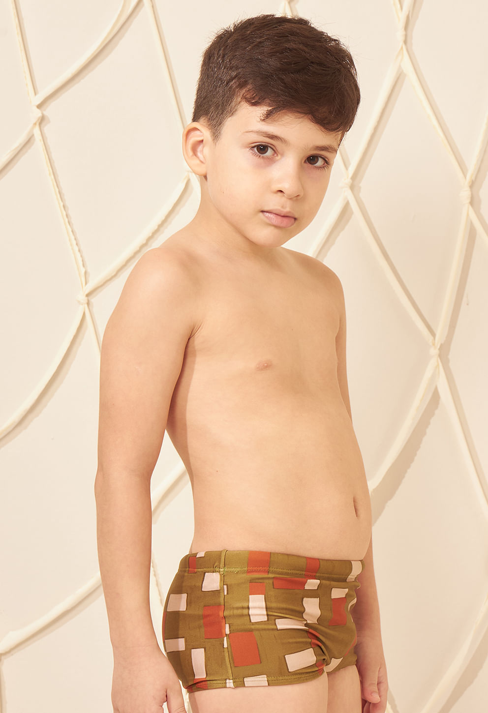 Criança de perfil usando sunga short infantil estampada em verde musgo, laranja e bege