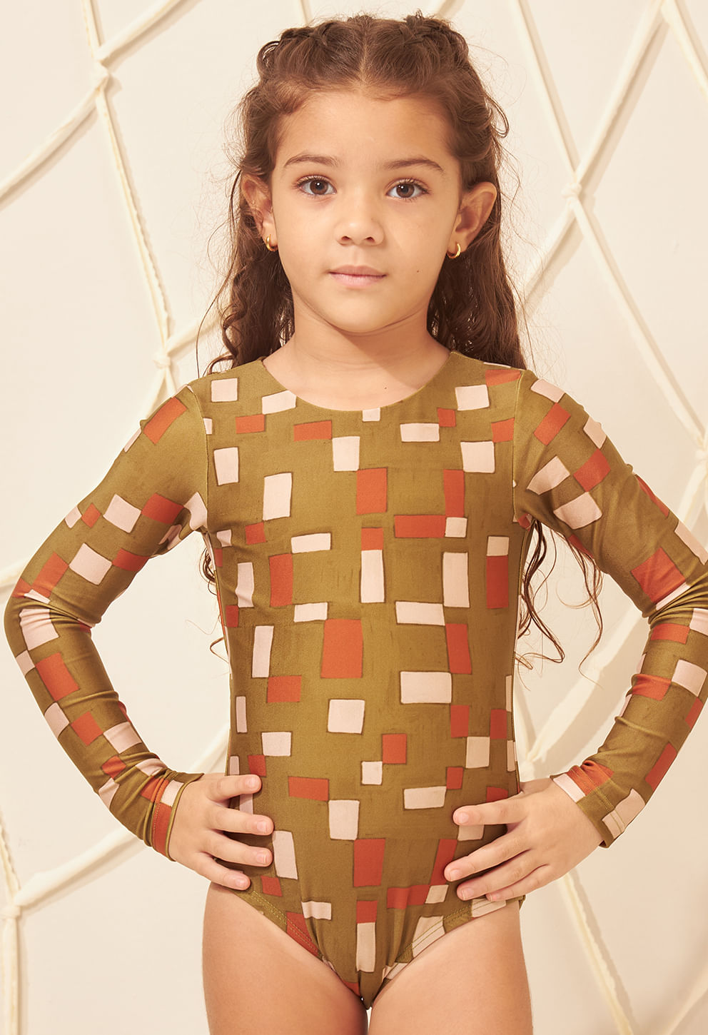 Imagem frontal de menina usando maiô infantil manga longa estampa geométrica verde oliva, laranja e bege