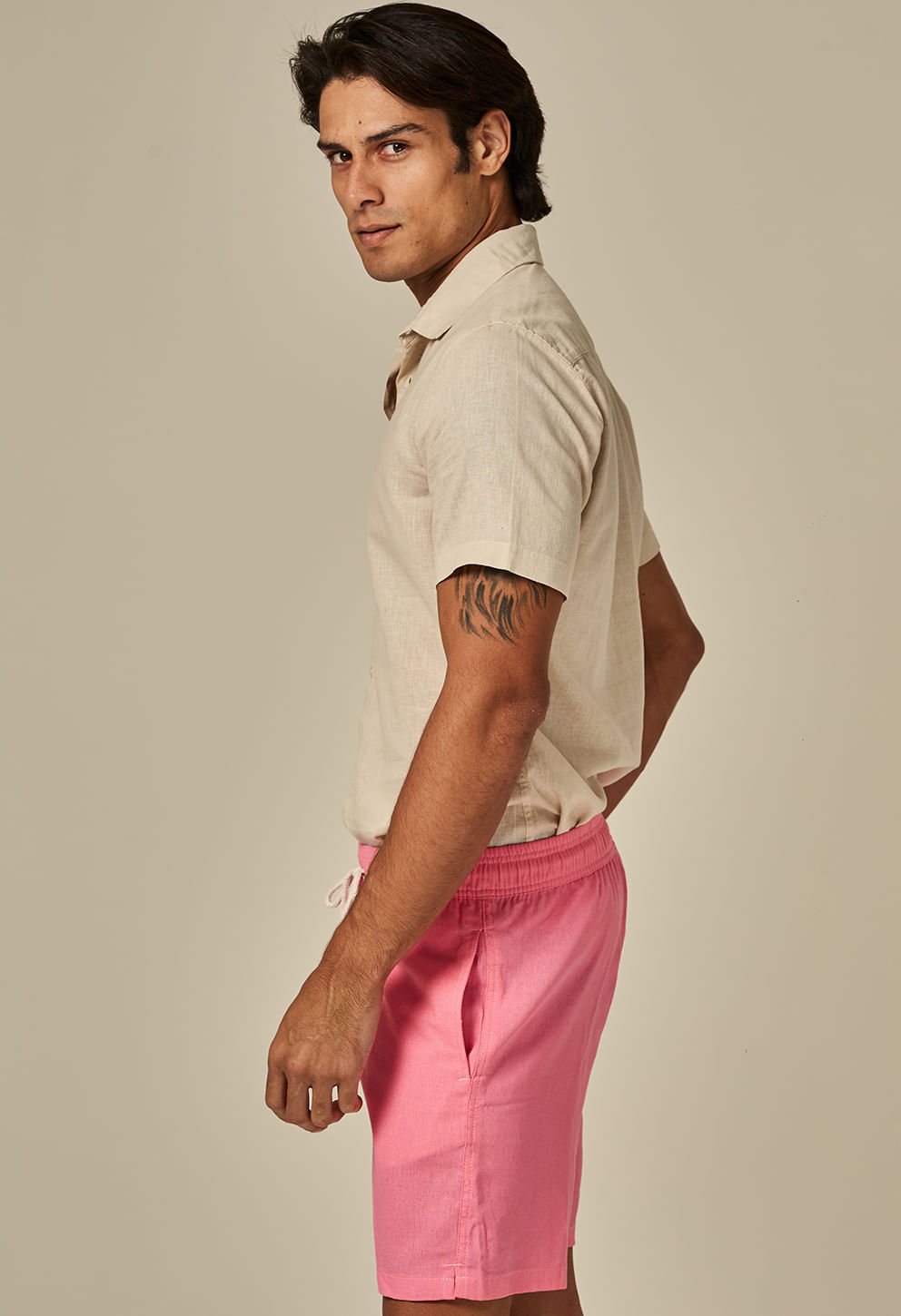 Homem vestindo bermuda casual de linho cor rosa pink com cós elástico e cordão branco, bolsos laterais e fundo neutro.