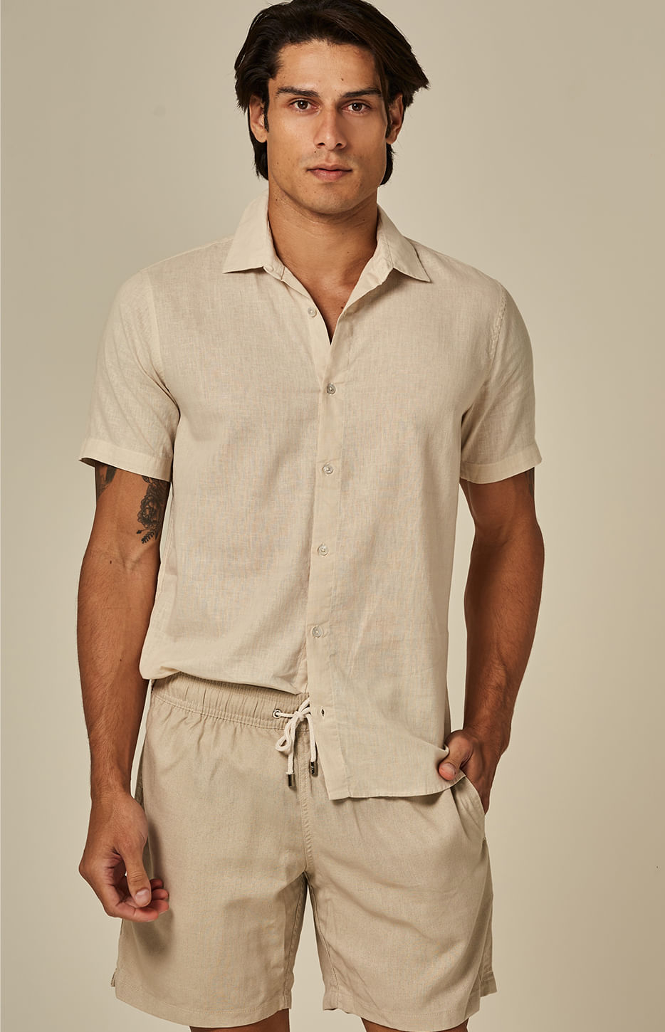 Homem usando bermuda casual bege claro de linho, com cordão na cintura e bolso lateral, em fundo neutro