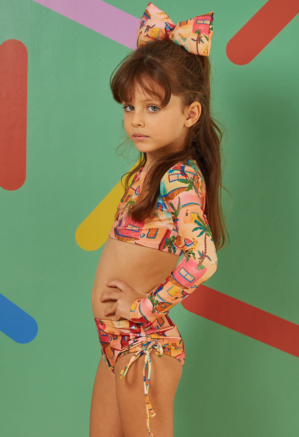 Menina em pose lateral vestindo biquíni infantil Valentina Castelo de Areia com estampa colorida