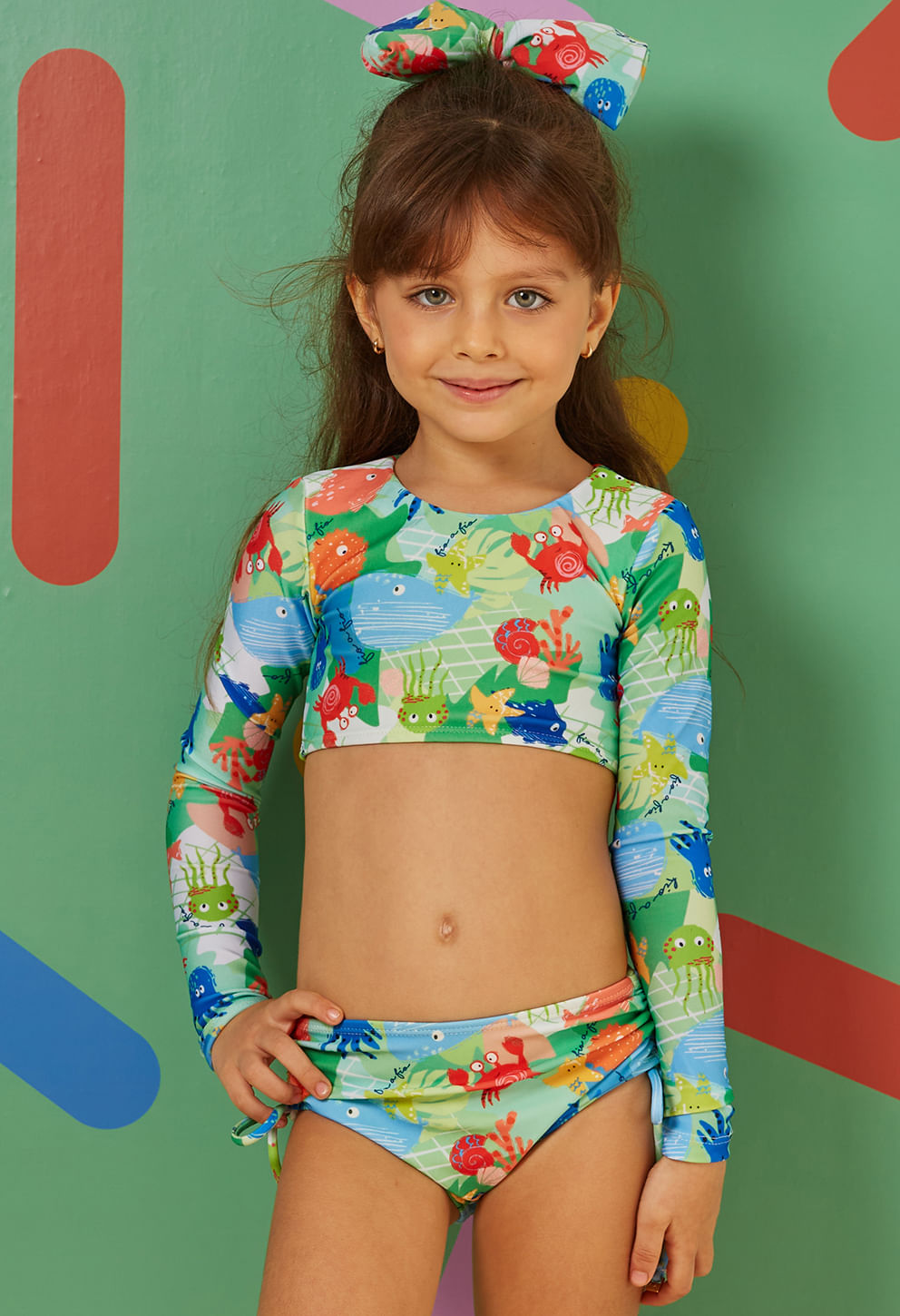 Menina sorridente usando biquíni infantil Valentina Moana com estampa colorida de animais marinhos em tons de verde, azul e vermelho
