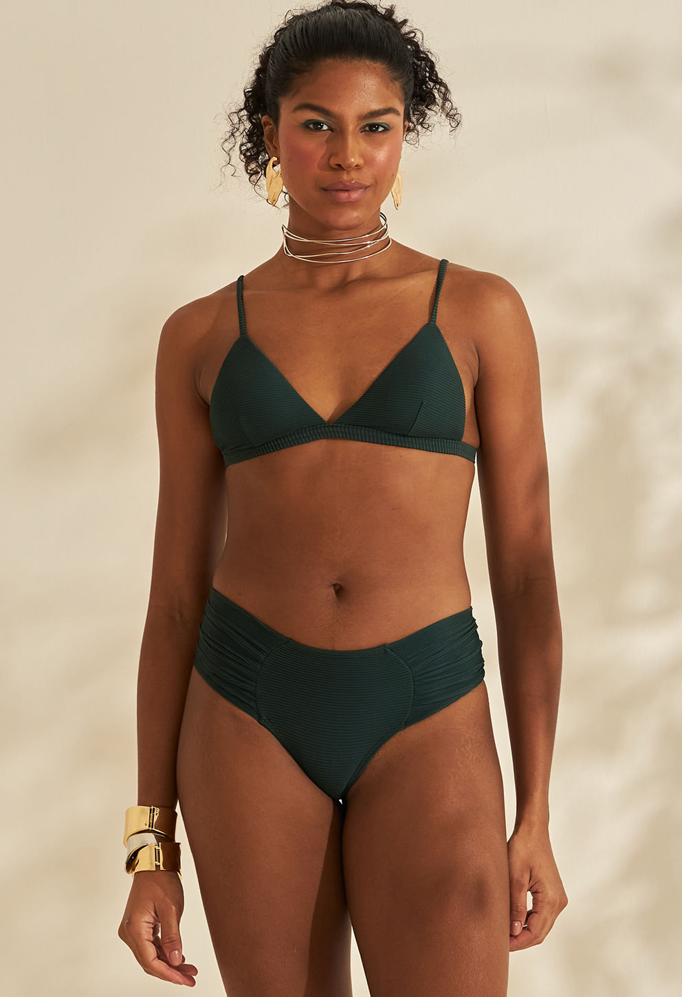 Frontal: modelo usando calcinha e top musgo cotelê, lateral larga franzida, acessórios dourados, fundo neutro