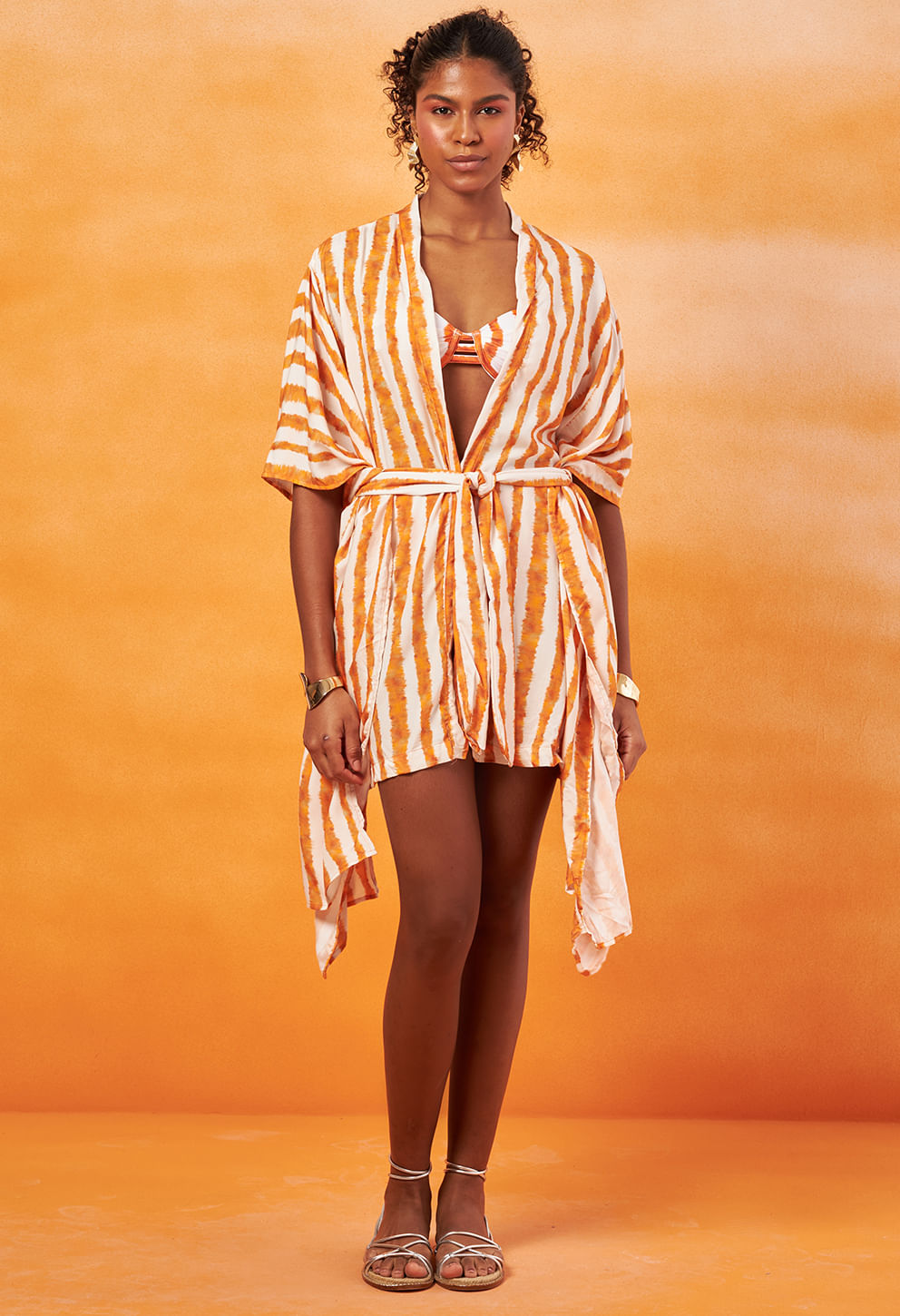 Kimono feminino curto listrado em tons laranja e off-white, caimento solto com faixa para amarração na cintura.