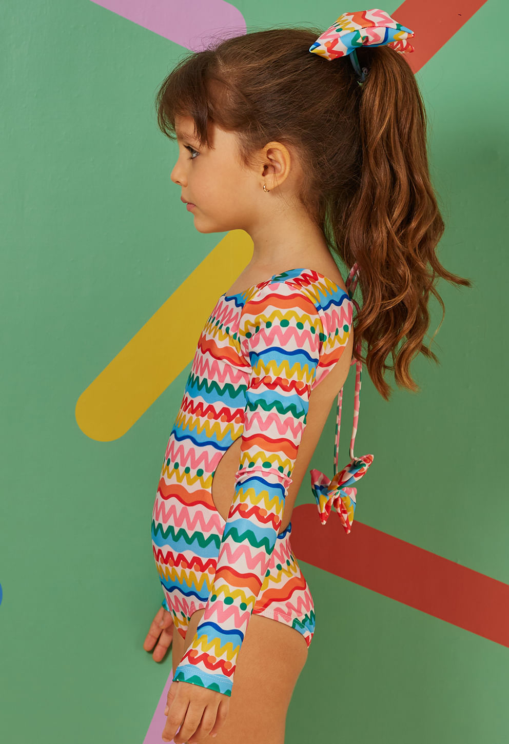 Perfil de menina com maiô manga longa multicolorido e laço nas costas