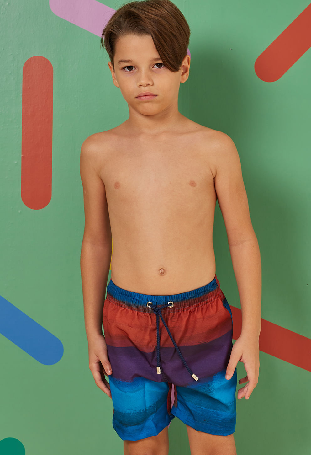 Foto frontal de criança vestindo bermuda infantil azul com faixas em vermelho, roxo e azul, cós elástico e cordão