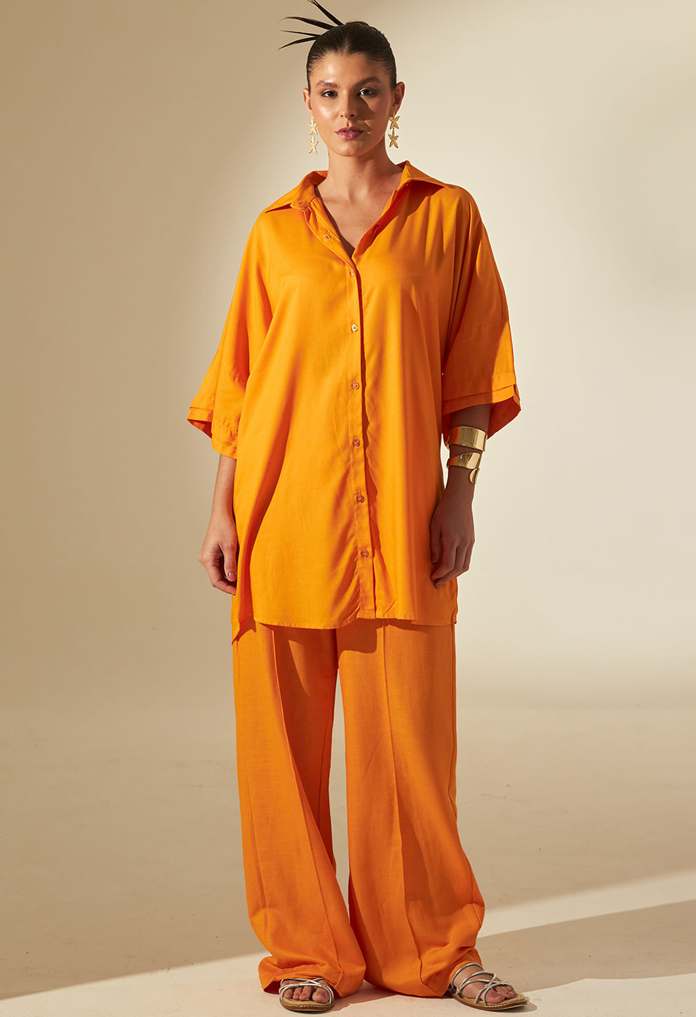 Modelo usando camisão longo laranja vibrante, abotoado, gola sport e mangas 3/4 volumosas
