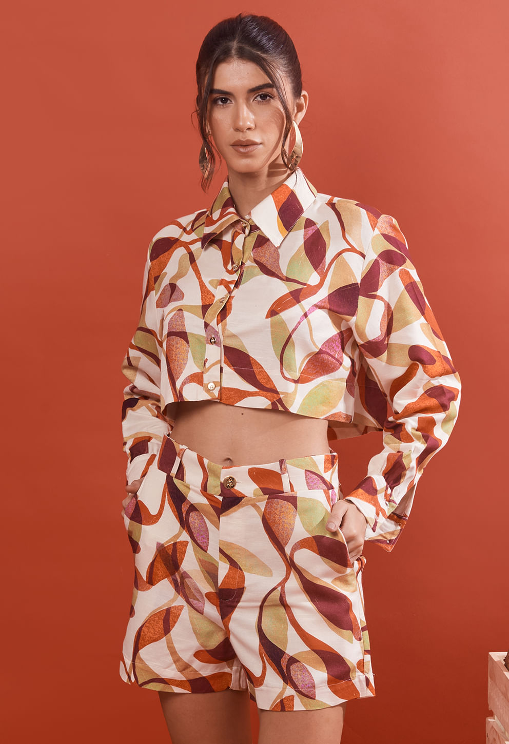 Cropped Carol Cajueiro frontal com estampa abstrata em tons de laranja, vinho, bege e verde claro