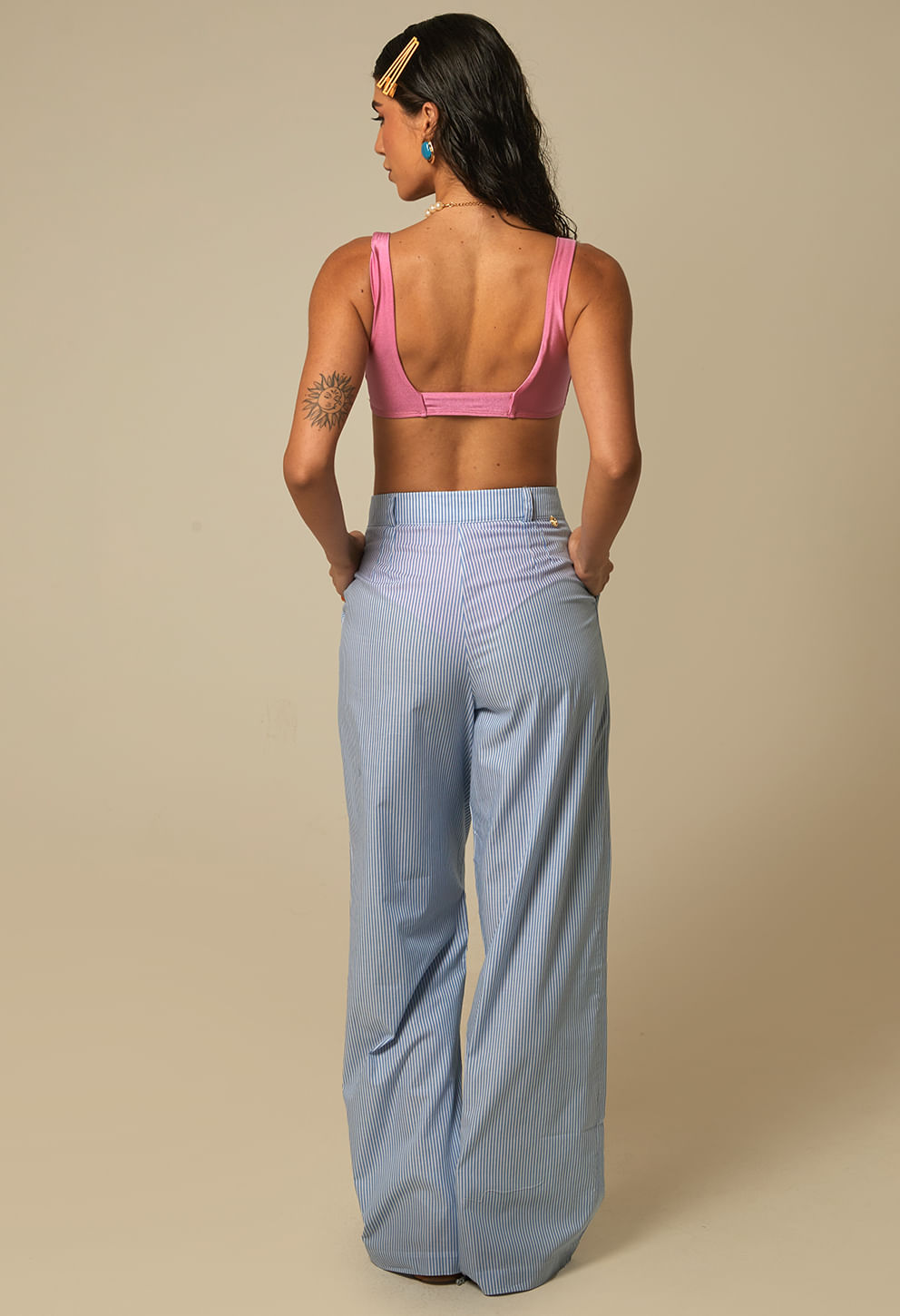 Vista traseira da calça pantalona listrada azul claro e branco mostrando cintura alta e pregas
