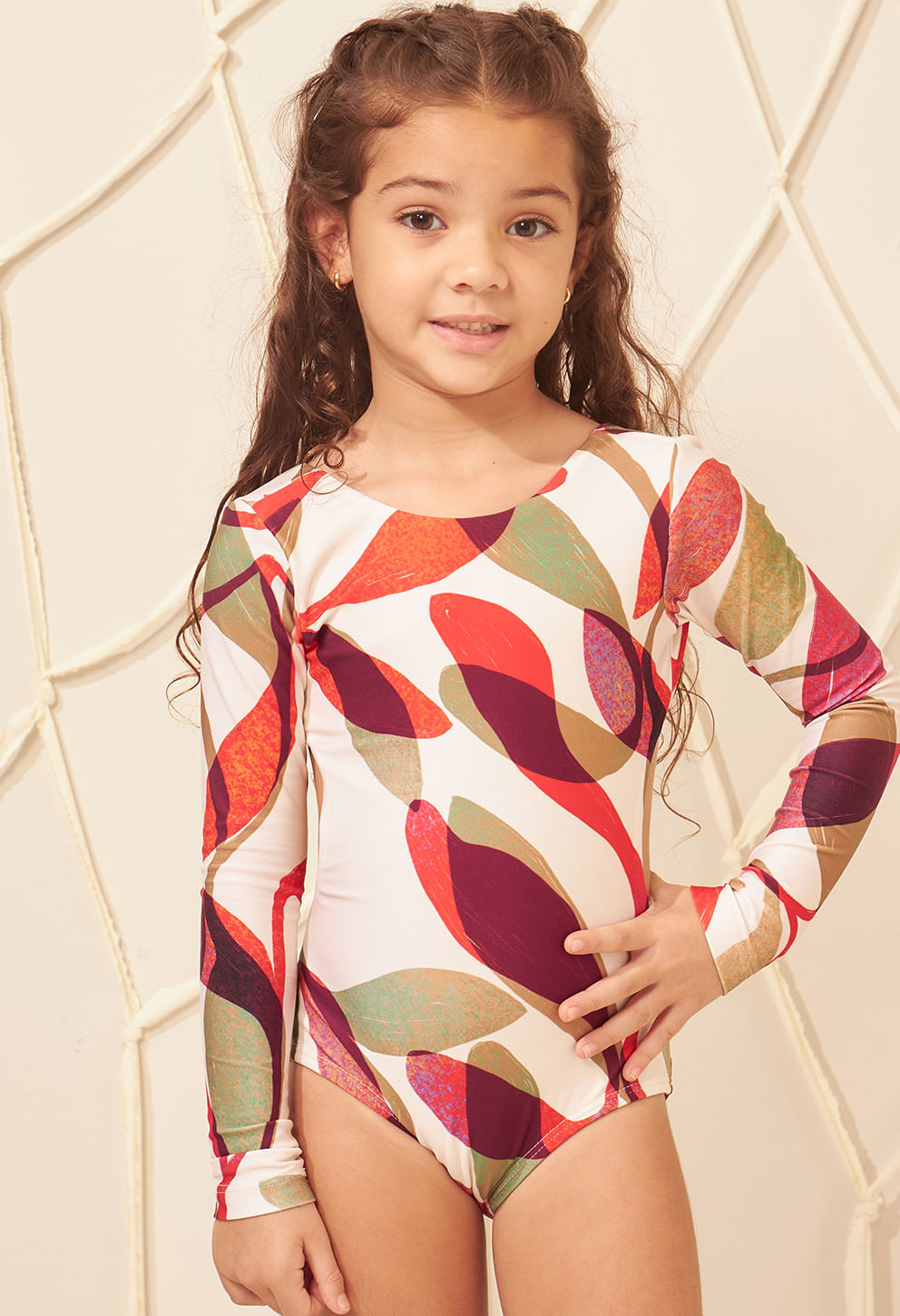 Menina vestindo maiô infantil manga longa com estampa de folhas em vermelho, vinho, verde e bege.