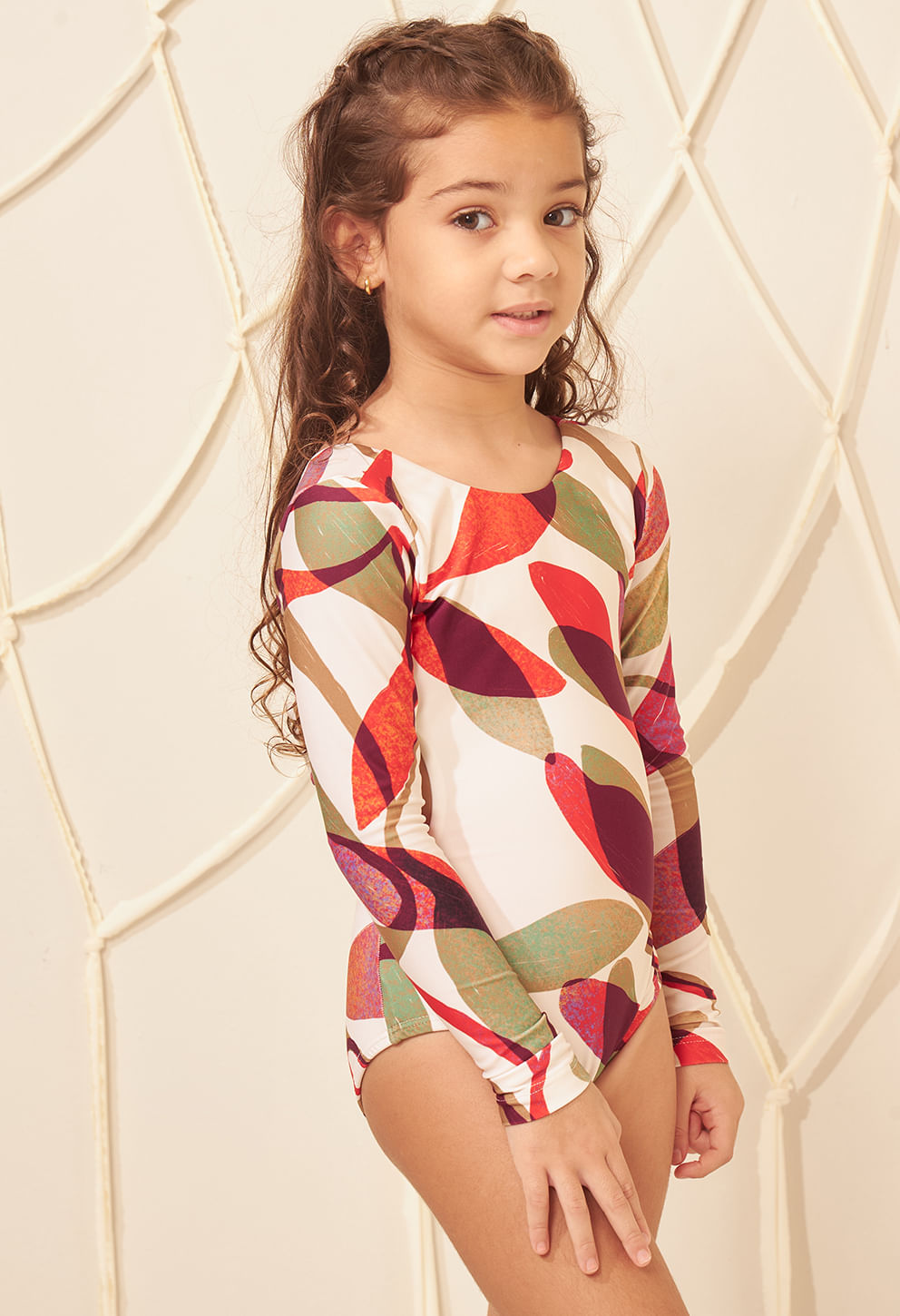 Menina de perfil usando maiô infantil manga longa com estampa de folhas, fundo neutro com cordas.