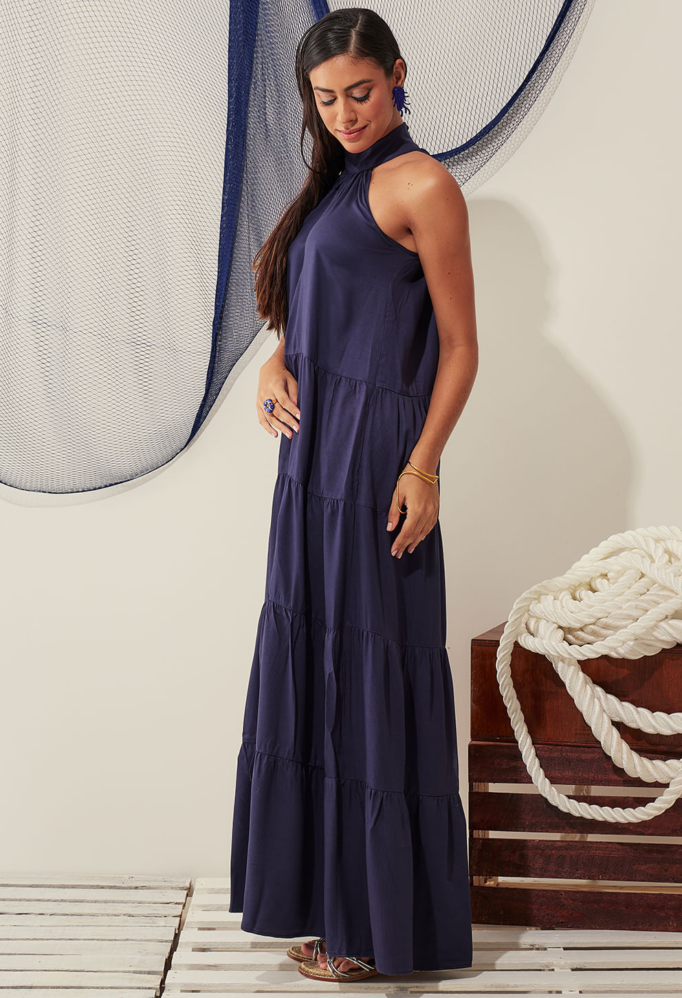 Vestido New Jasmin Alto Mar visto de lado, gola alta, camadas com pregas horizontais, cenário praia/cidade