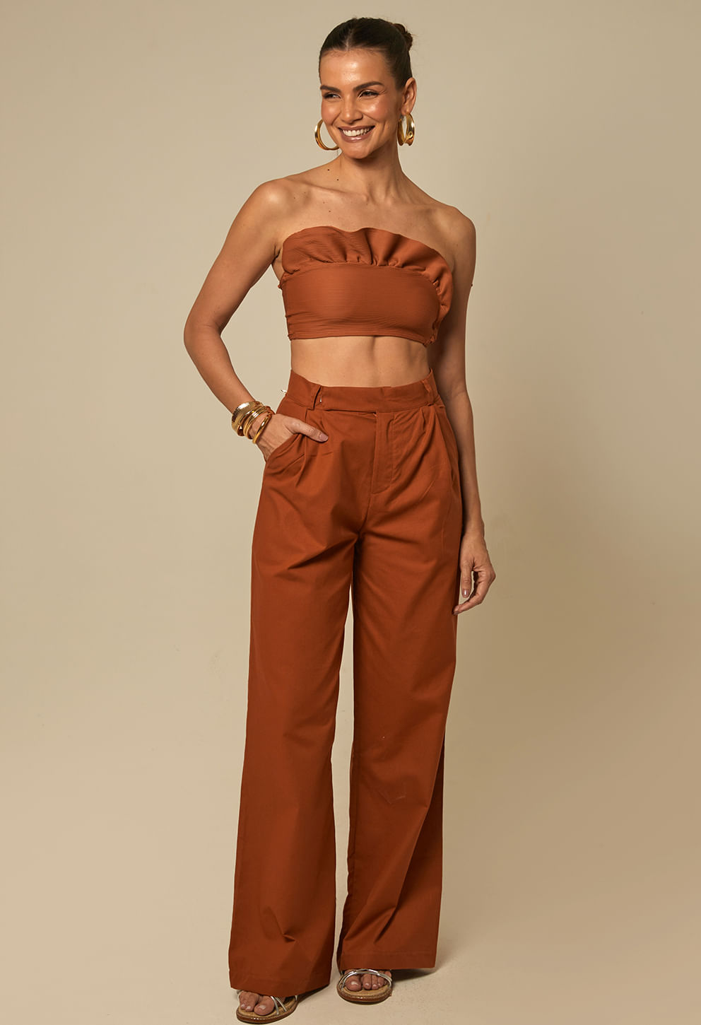 Mulher sorridente usando calça pantalona de cintura alta na cor terracota, estilo largo e tecido com caimento leve.