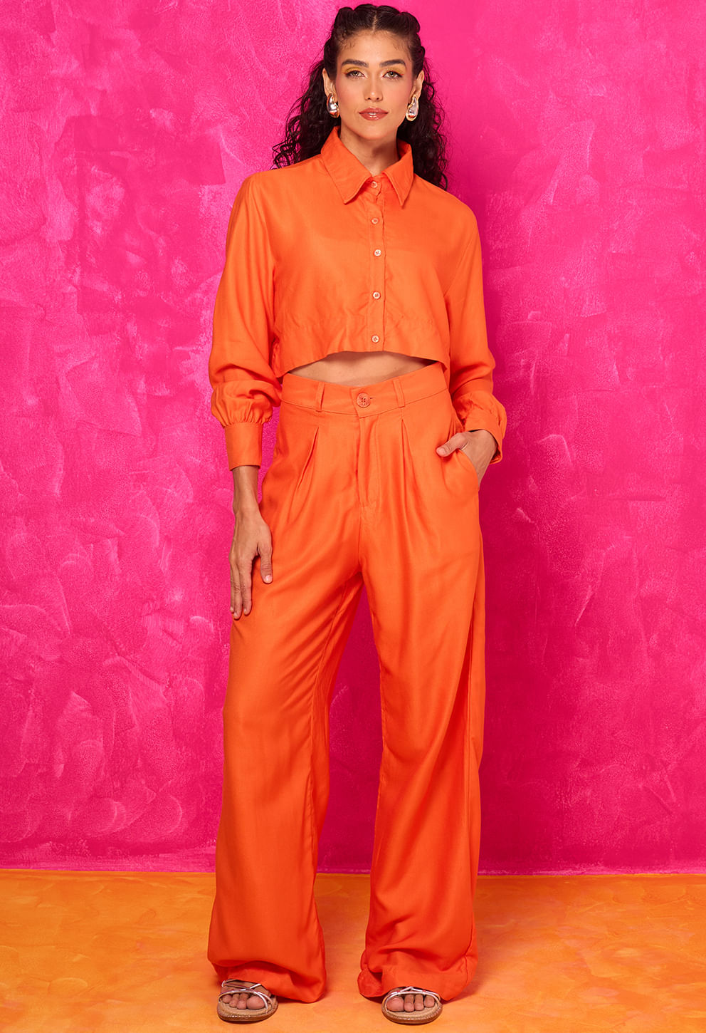 Mulher vestindo cropped laranja com gola e botões frontais, manga longa e calça laranja de cintura alta