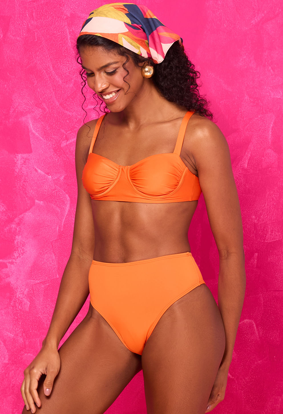 Modelo sorridente usa calcinha Hot Beatriz Bossa laranja vibrante, mostrando cintura alta e corte cavado.