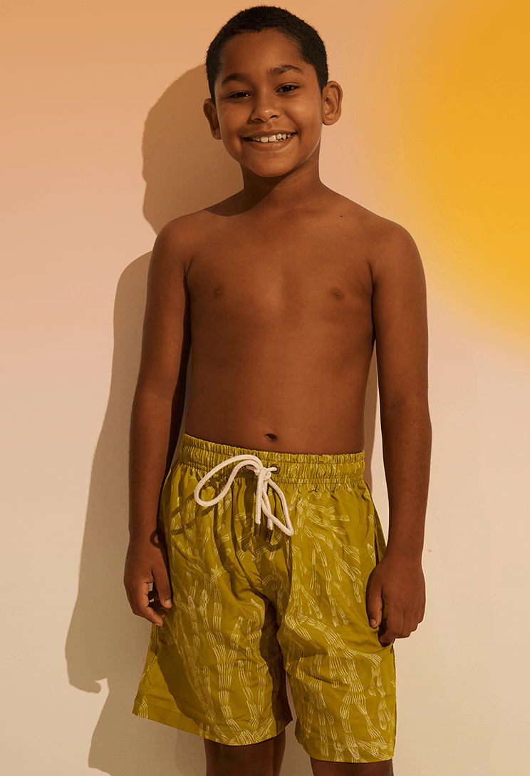 Menino sorridente de frente usando bermuda infantil verde com estampa de corais brancos