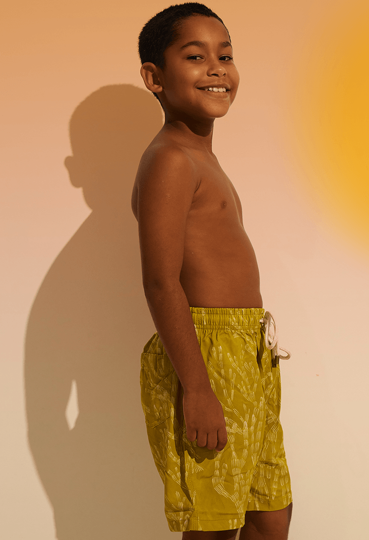 Menino de perfil vestindo bermuda infantil verde com estampa de corais brancos
