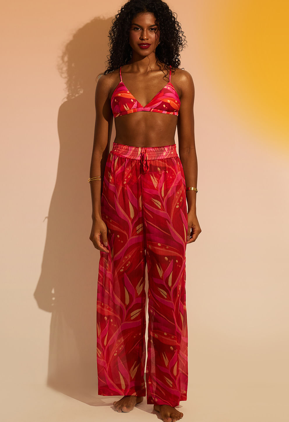 Modelo usando calça pantalona rosa fluida com cós elástico e cordão, tecido leve e transparente
