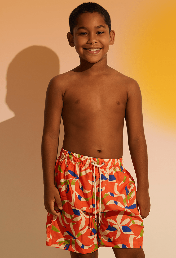 Menino sorridente usando bermuda infantil laranja com estampa colorida, cós elástico e bolso traseiro